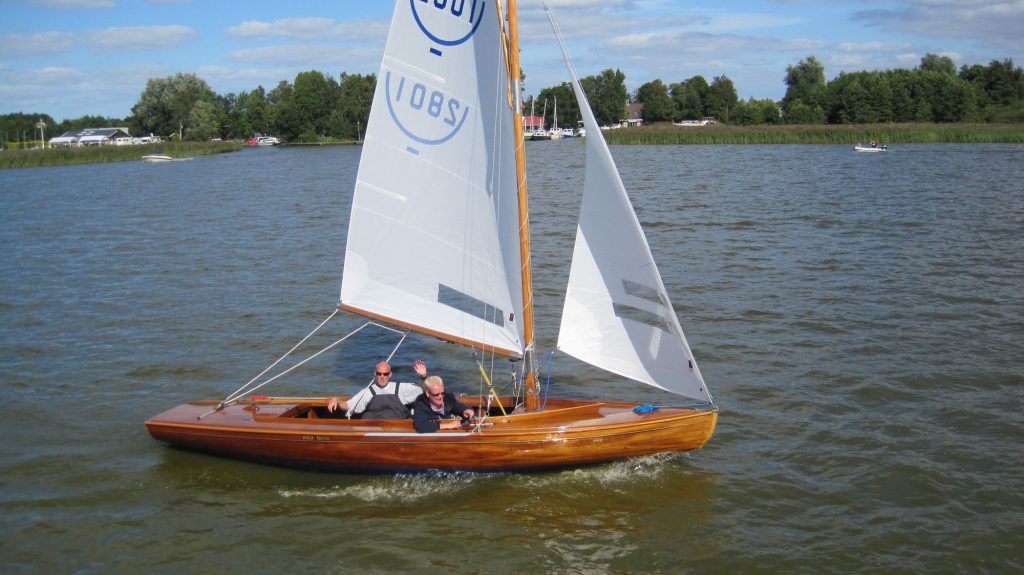 Twee zeilers in een houten zeilboot zwaaien
