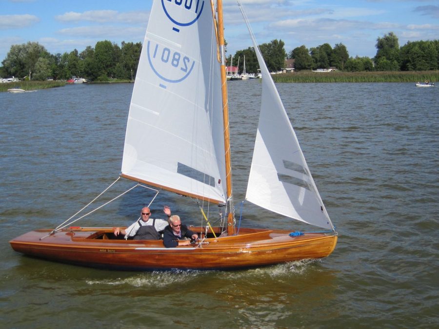 Twee zeilers in een houten zeilboot zwaaien