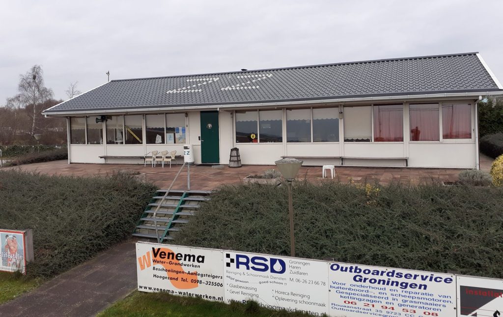 Wit clubhuis met grijs dak en sponsorborden
