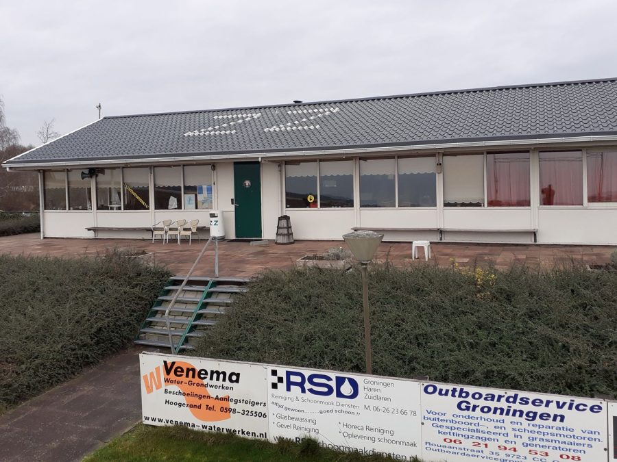 Wit clubhuis met grijs dak en sponsorborden