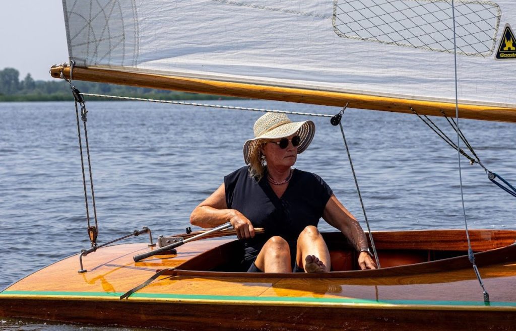 Zeilster met zonnehoed aan het roer van een houten boot