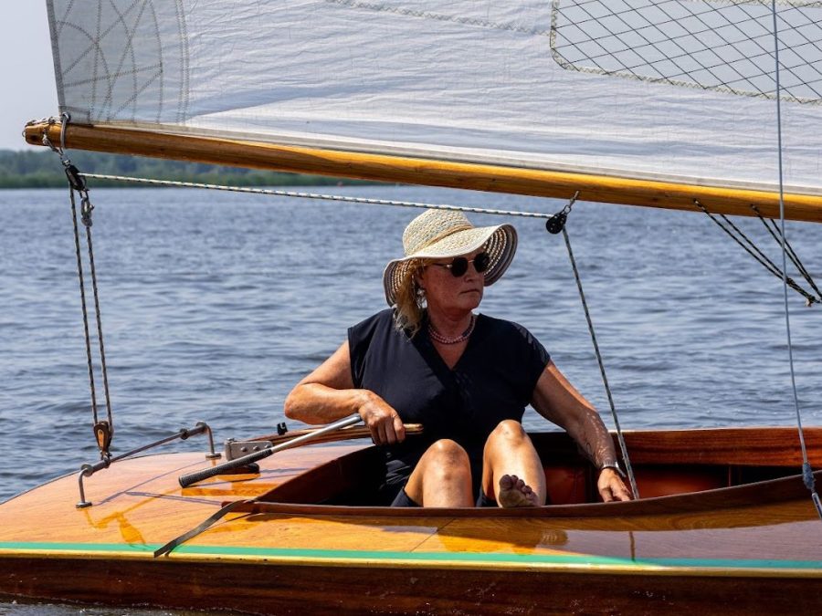 Zeilster met zonnehoed aan het roer van een houten boot