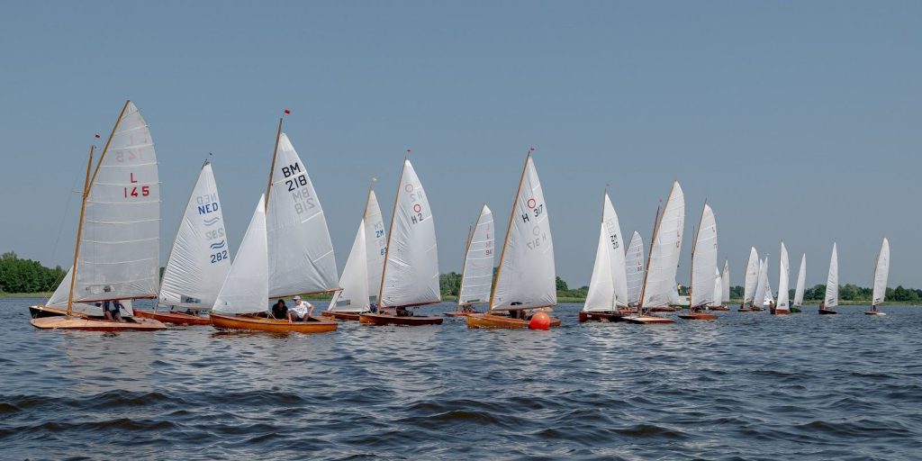 Een rij houten zeilboten naast elkaar op het water