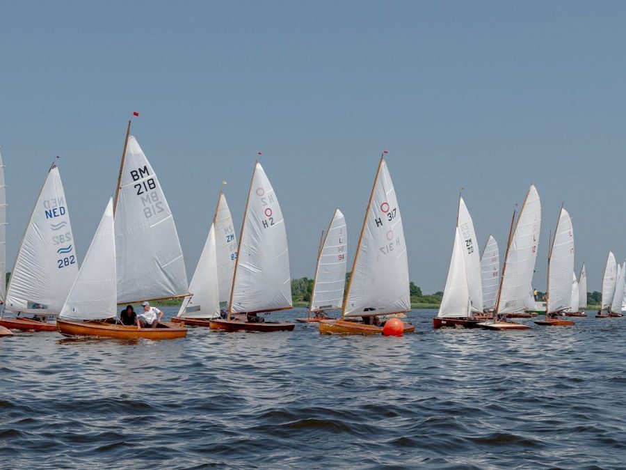 Een rij houten zeilboten naast elkaar op het water
