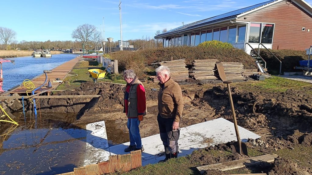 Twee vrijwilligers bij werkzaamheden aan de waterkant voor het clubhuis