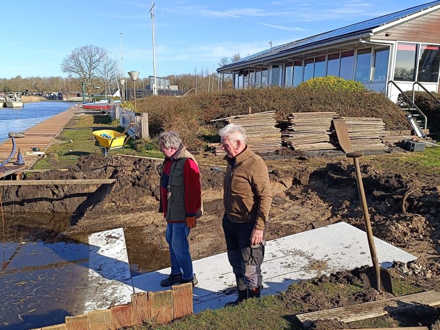 Twee vrijwilligers bij werkzaamheden aan de waterkant voor het clubhuis