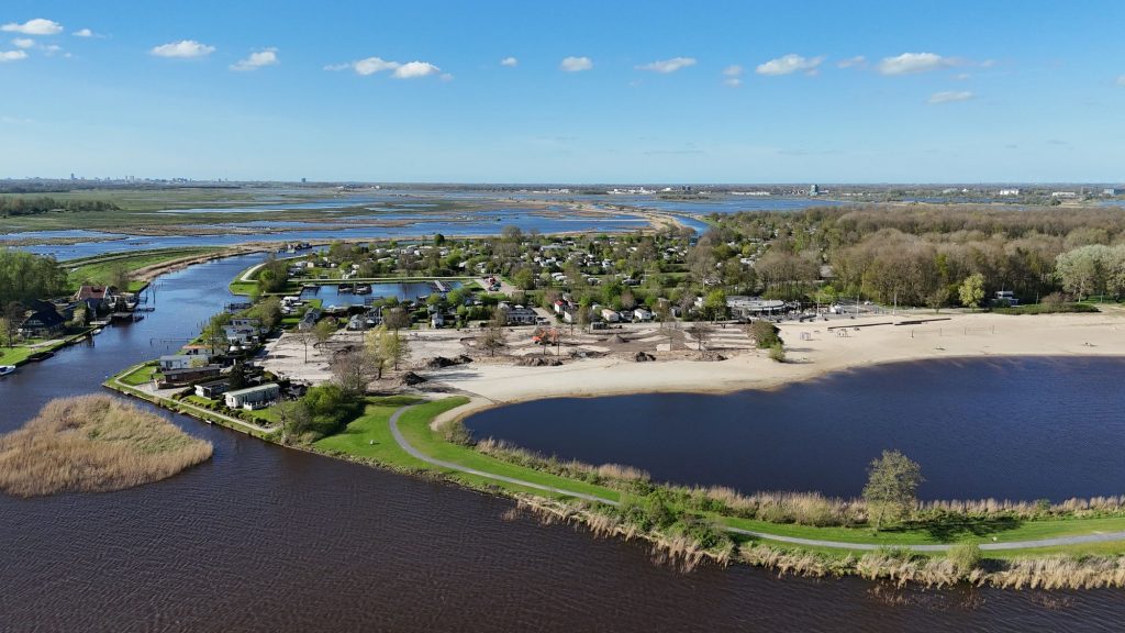 Luchtfoto van een meer met strand, bos en weilanden