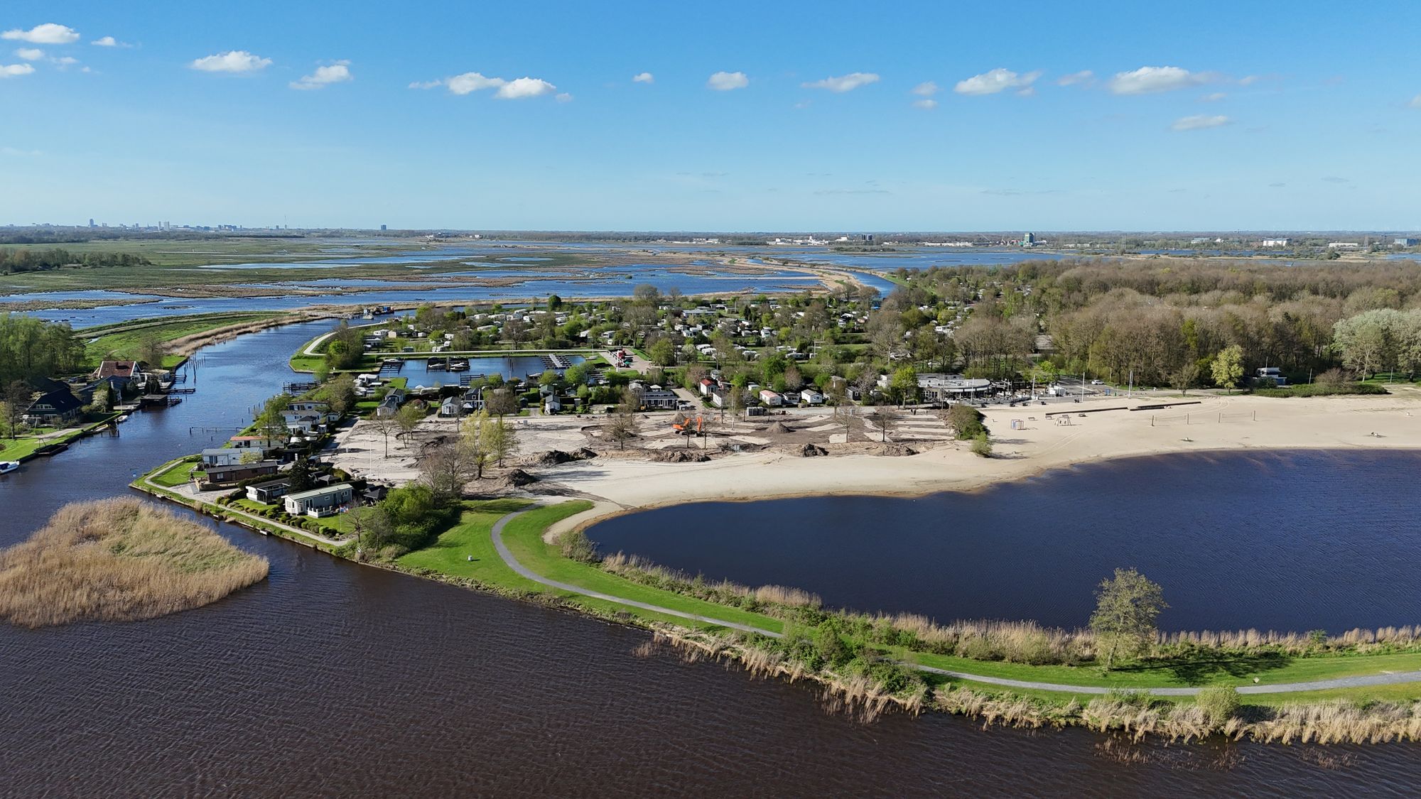 Luchtfoto van een meer met strand, bos en weilanden