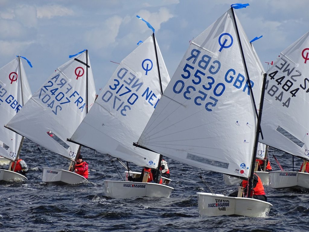 Een groep Optimist-zeilbootjes dicht bij elkaar