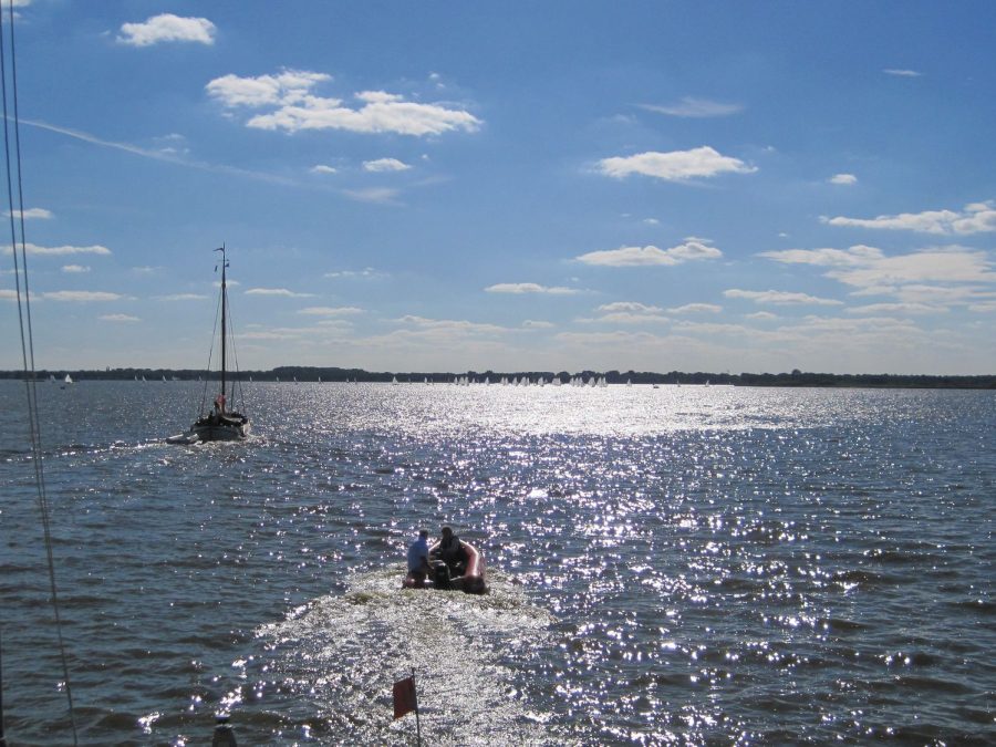 Zonlicht glinstert op het meer, op de achtergrond een zeilboot